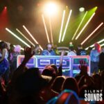 DJ Booths, Holograms & Lighting (2) A DJ host using the DJ booth for a party event with a crowd dancing behind them nighttime